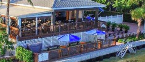 Ein Restaurant am Wasserufer mit Terrassensitzgelegenheiten, einem überdachten Bereich und Blick auf das Wasser.