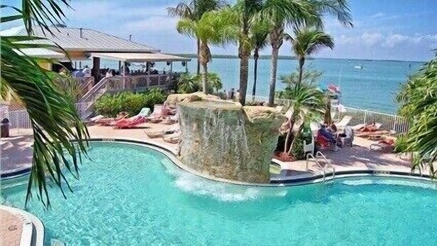Una piscina con una formación rocosa, sillas de descanso y vistas al océano.