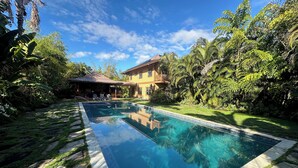 Una piscina rectangular con agua azul cristalina, rodeada por un borde de piedra y una zona cubierta de césped.