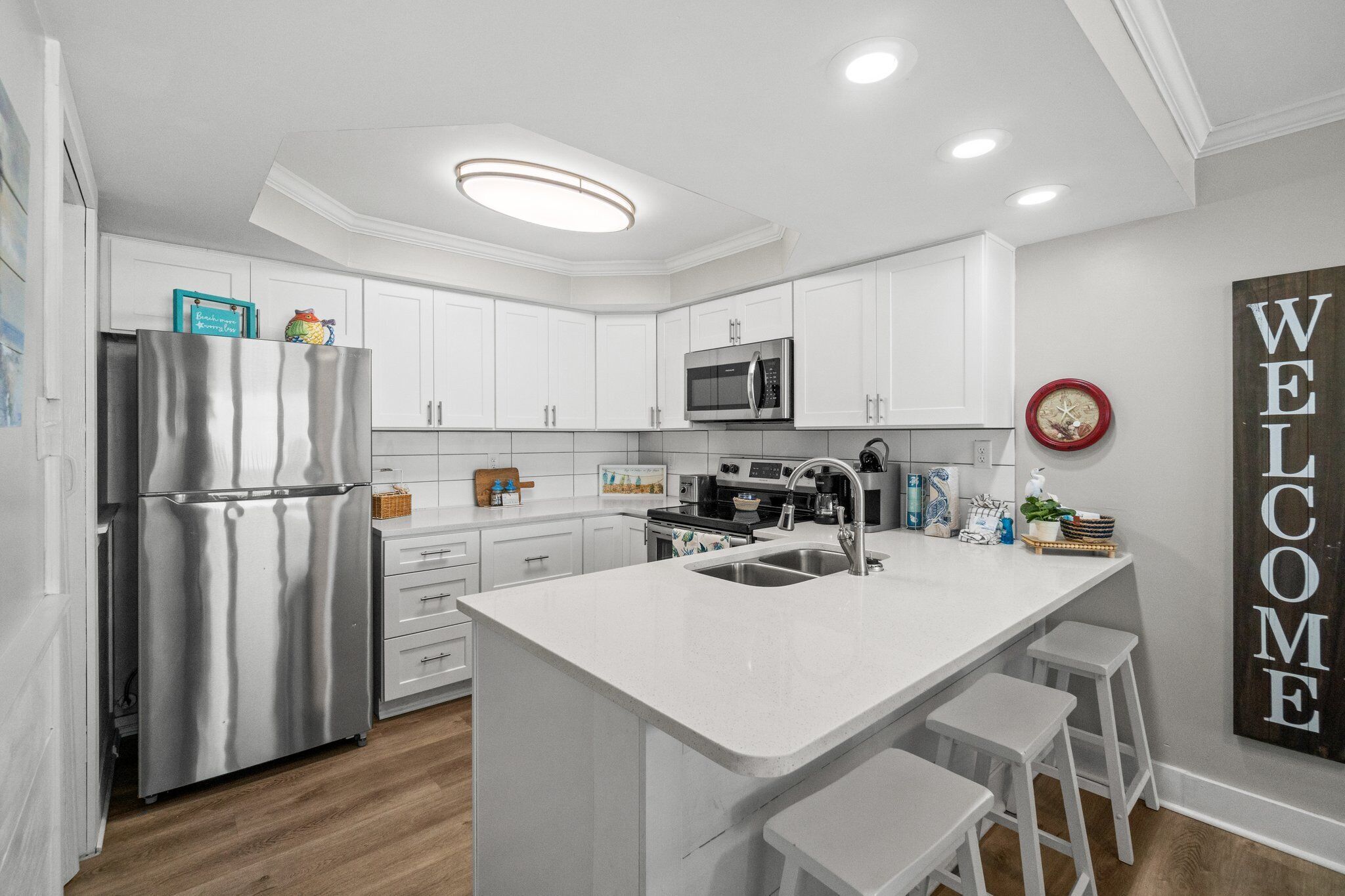 A modern kitchen with white cabinetry, stainless steel appliances, and a central island with bar stools.