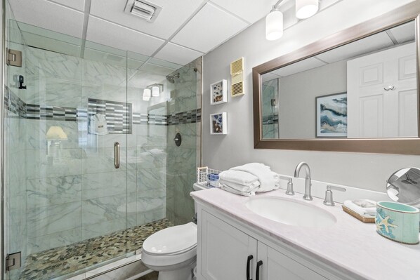 A modern bathroom with a glass-enclosed shower, a white sink, and a large mirror. - Beach Lovers Welcome! Gulf Front Condo PW403 (Panama City Beach)