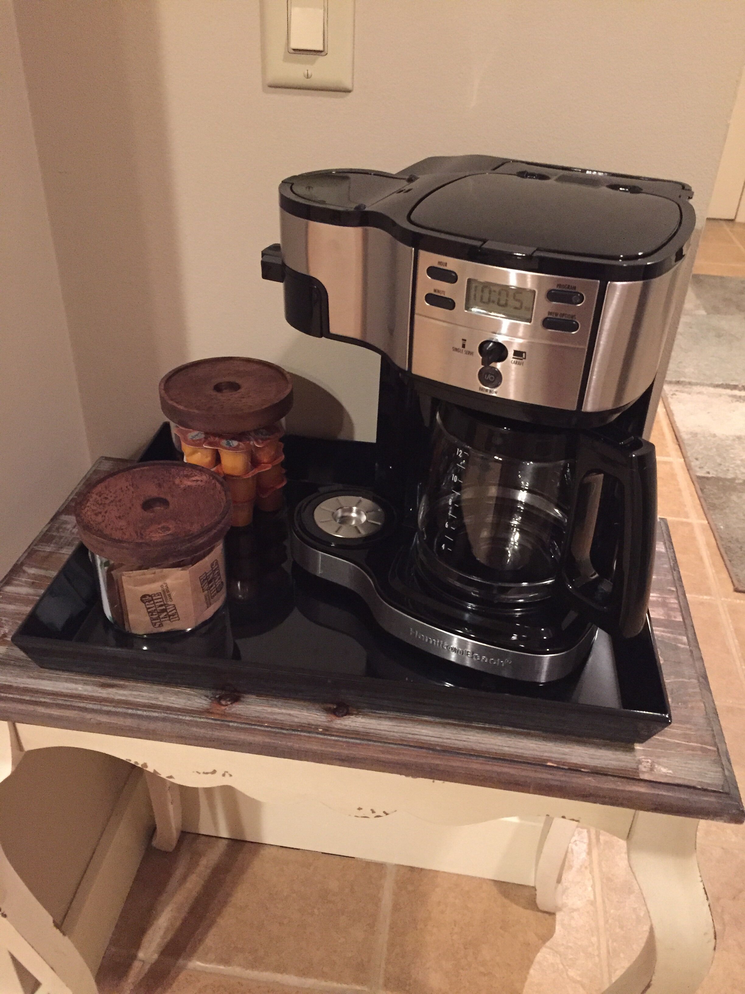 A coffee maker on a countertop with a tray, a jar, and a container.