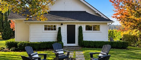 A white house with a front porch, four Adirondack chairs, a fire pit, and a stone pathway.