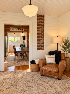 A living room with a leather sofa, a dining area with a table and chairs, a kitchen with a refrigerator, and a sign that reads 'GROCERY'.