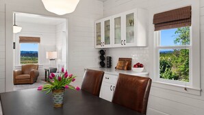 A dining area with a table, chairs, a vase of flowers, and a view of greenery outside. - Snohomish Fobes Farmhouse built:1918  (Snohomish)
