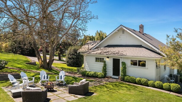 A single-story house with a sloped roof, a chimney, and a well-maintained lawn with outdoor furniture. - Snohomish Fobes Farmhouse built:1918  (Snohomish)