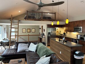 Una cocina moderna con electrodomésticos de acero inoxidable, una zona de comedor de madera y un dormitorio superior con vistas.