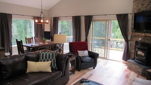 A spacious living room with a fireplace, a dining area, and large windows offering a view of the outdoors. - Custom home in St Mary’s Glacier (Idaho Springs)