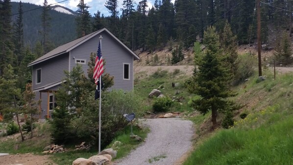 A house with a gravel driveway, surrounded by trees and a mountainous backdrop. - Custom home in St Mary’s Glacier (Idaho Springs)