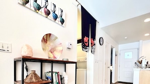 A hallway with a wooden floor, a bookshelf with various items, a wall-mounted painting, and a door with a curtain. - Modern 2 Bedrooms, 1 Bathroom Apartment (Fort Collins)