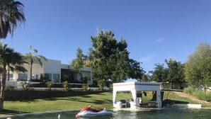 A pool area with a jet ski, a gazebo, and a modern building in the background. - River Front guest house with Ramp, Beach, Volleyball, and Gazebo on the Water (Big River)