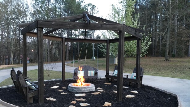A gazebo with a fire pit in the center, surrounded by a stone border and benches.