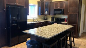 A kitchen with dark wooden cabinets, a granite countertop, a black refrigerator, a microwave, and a stove.