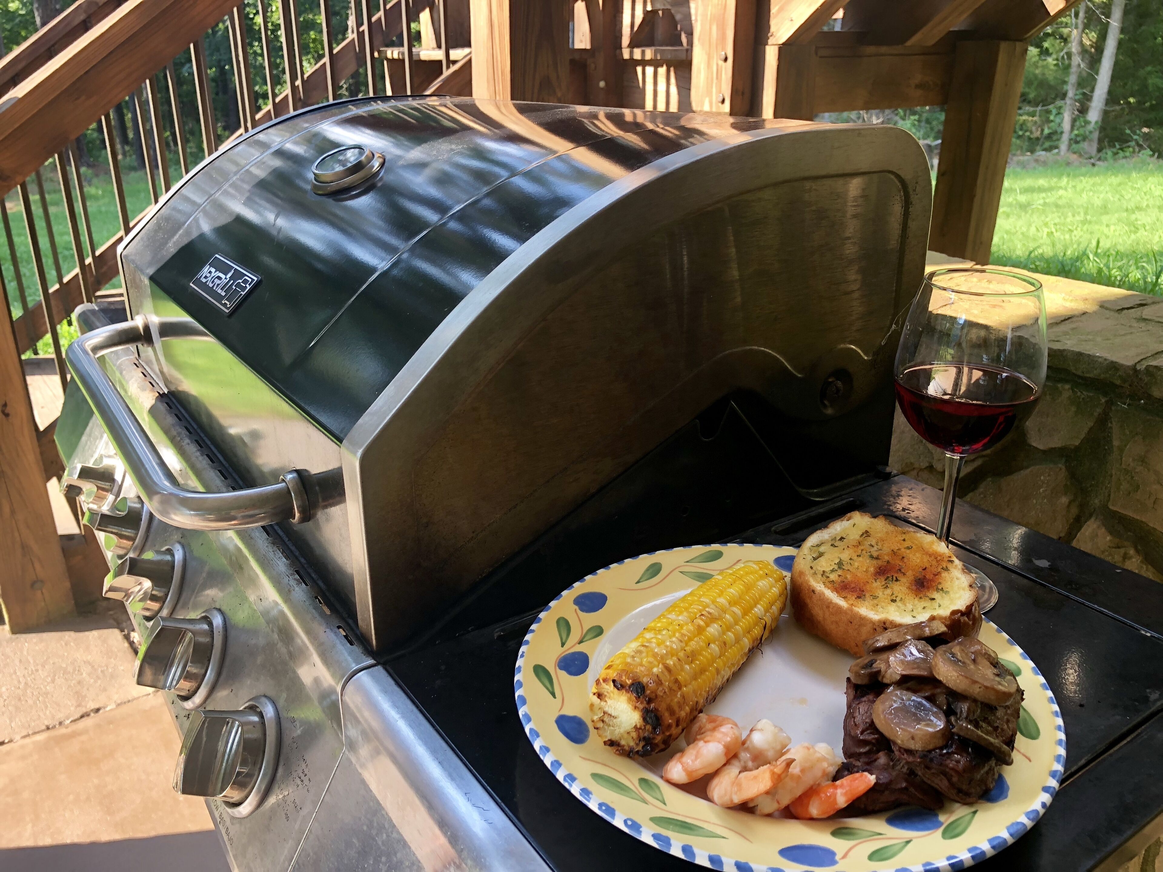 Ein Grill mit einer Platte Essen und einem Glas Rotwein auf einer Terrasse.