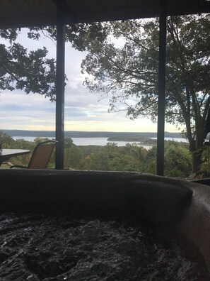 Ein Zimmer mit Blick auf einen See und Bäume. Im Vordergrund stehen ein Sessel und ein Tisch.