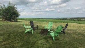 A grassy outdoor area with three Adirondack chairs and a fire pit.