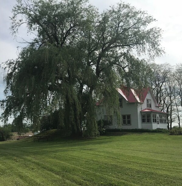 A white house with a red roof, surrounded by a grassy lawn and large trees.