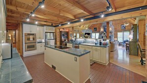 A spacious kitchen with wooden beams, a large island, and a stone accent wall.