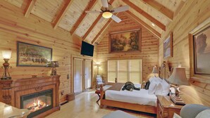 A cozy log cabin bedroom with a fireplace, a bed, a sofa, and a ceiling fan.