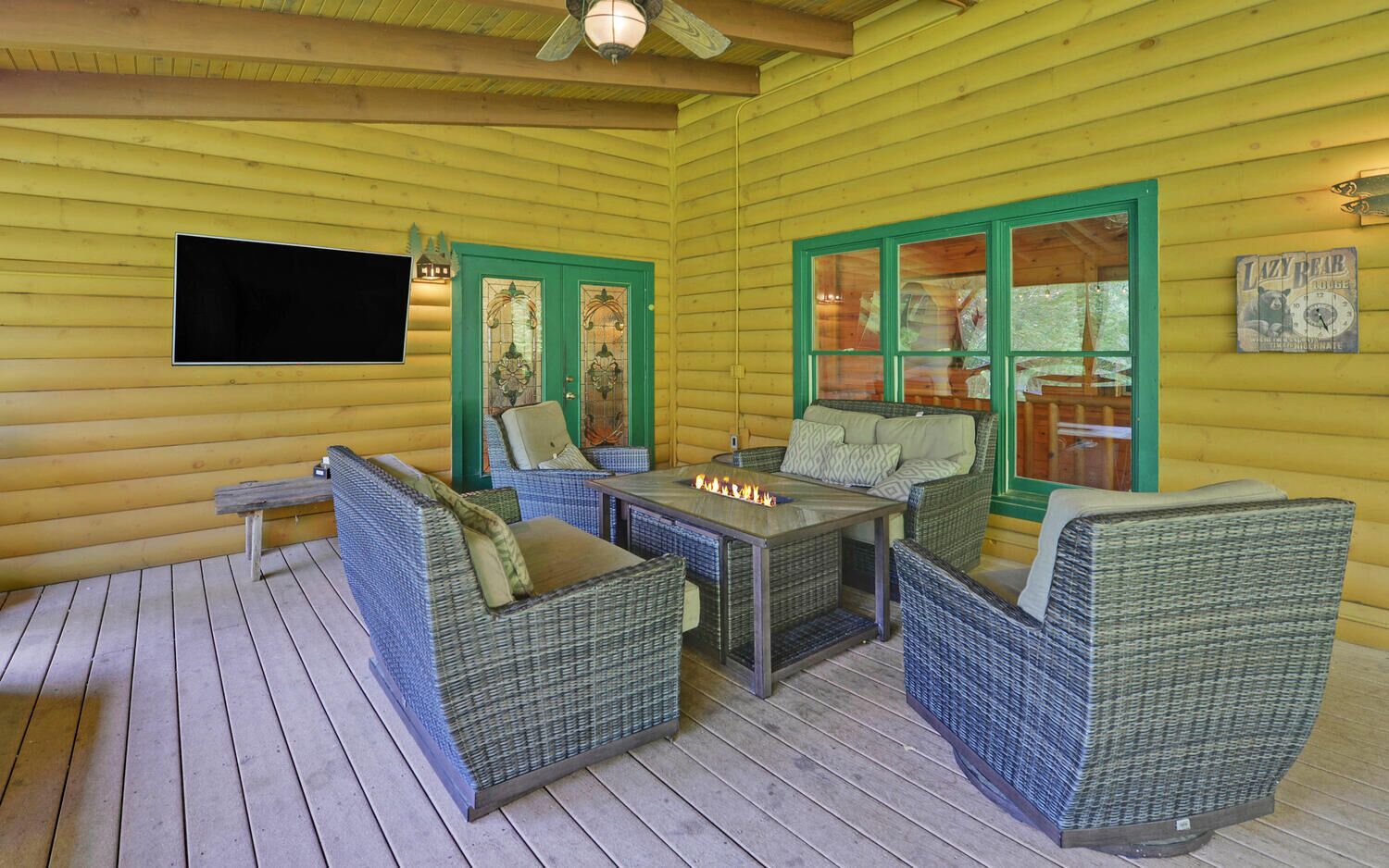A cozy outdoor seating area with wicker furniture, a fire pit, and green-framed windows.