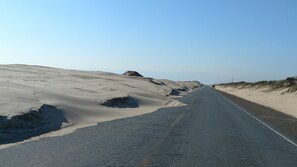 Estrada ladeada por dunas de areia sob um céu limpo.