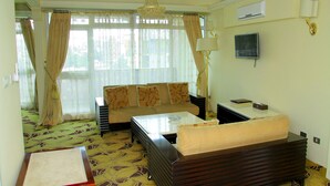 Quarto de hotel com sofá, mesa de centro, televisão e lustre.