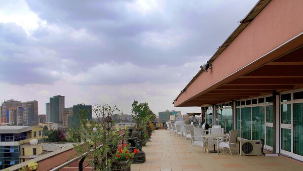 Terraço no telhado com área de estar externa, vista para o horizonte urbano e um edifício com grandes janelas.