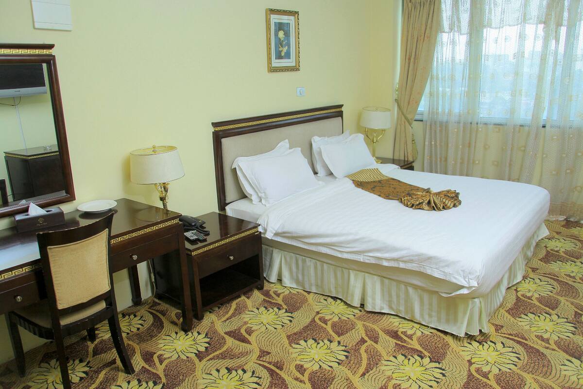 Habitación de hotel con cama, escritorio, silla, televisor y ventana con cortinas.