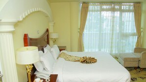 Quarto de hotel com uma cama grande, uma escrivaninha com abajur, telefone e uma cadeira.
