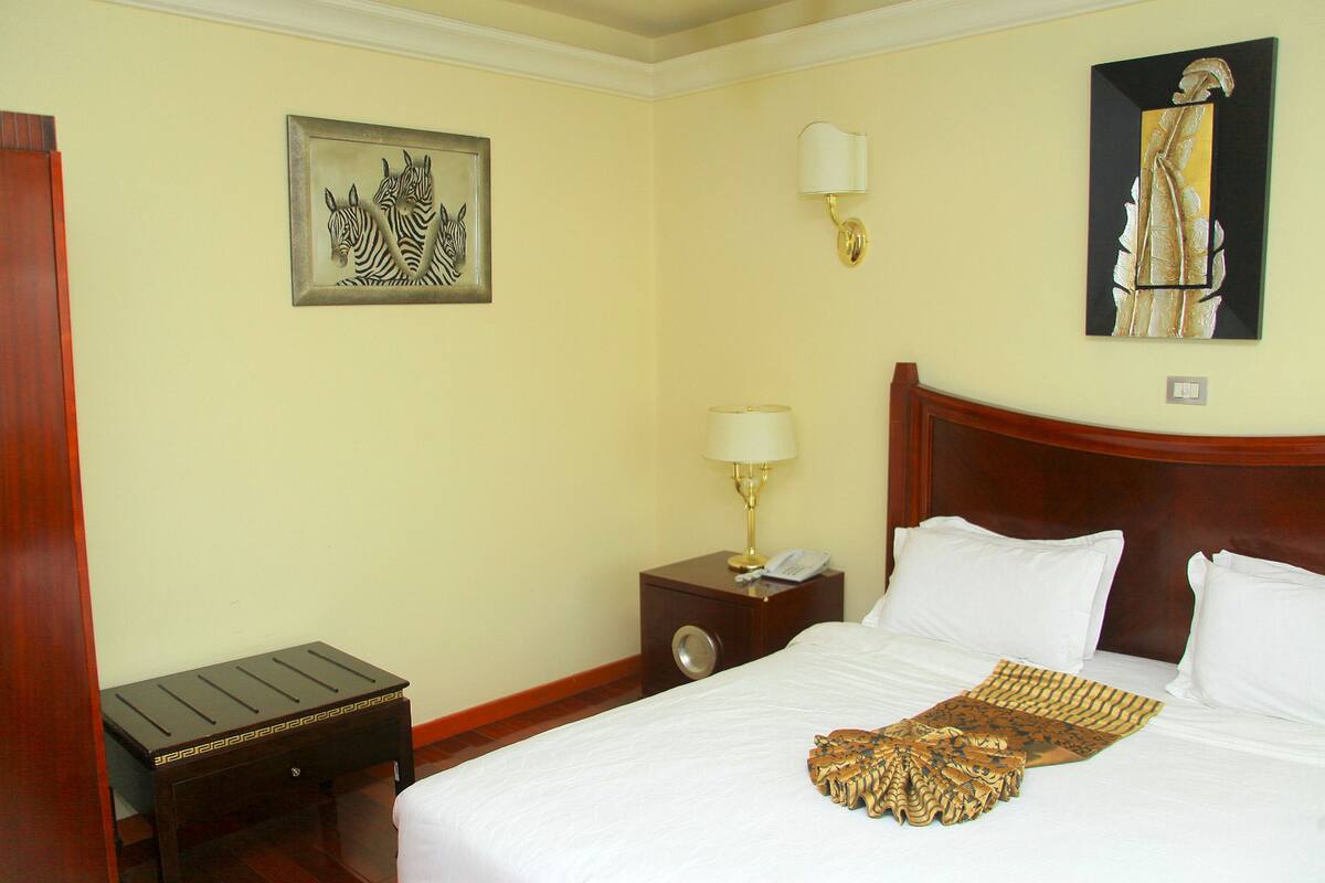 Una habitación de hotel con una cama, una mesita de noche con lámpara, una obra de arte con cebra enmarcada y un cojín decorativo.