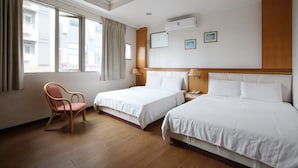 Et hotelværelse med to senge, en træstol, et vindue med gardiner og en vægmonteret aircondition.
