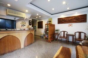 Zona de recepción de un hotel con un mostrador de madera, un televisor y una pieza decorativa china tradicional en la pared.