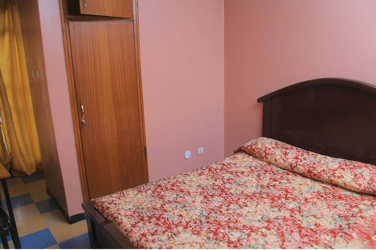 Un dormitorio con un armario de madera, una cama con colcha floral y suelo a cuadros.