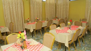 A dining area with multiple tables set with red and white checkered tablecloths, wicker chairs, and floral centerpieces. - Yonas Hotel (Addis Ababa)