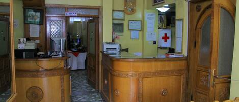 A reception area with a wooden reception desk, a clock, and various signs including a reception sign and an exit sign.