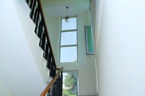 A staircase with a wooden handrail and black balusters, leading to a room with a large window and a green-framed picture frame on the wall. - Tseder Pension (Addis Ababa)