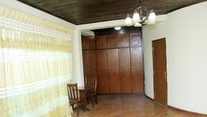 A room with wooden flooring, a wooden wardrobe, a wooden table with chairs, and a red rug. - Tseder Pension (Addis Ababa)