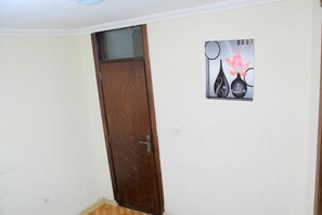 A closed wooden door with a glass panel, a wall-mounted artwork of vases with flowers, and a light switch.