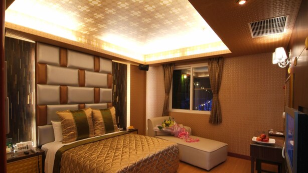 A modern hotel room with a large bed, a small sofa, a desk, and a window with a view of the city lights. - Cai-Lai Hotel (Taoyuan City)