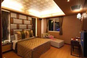 Une chambre d’hôtel moderne, dotée d’un grand lit, d’un petit canapé, d’un bureau et d’une fenêtre offrant une vue sur les lumières de la ville.