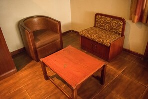 A small room with a wooden chair, a wooden table, and a sofa with a patterned cushion. - Chelsea Suites Limited (Lagos)