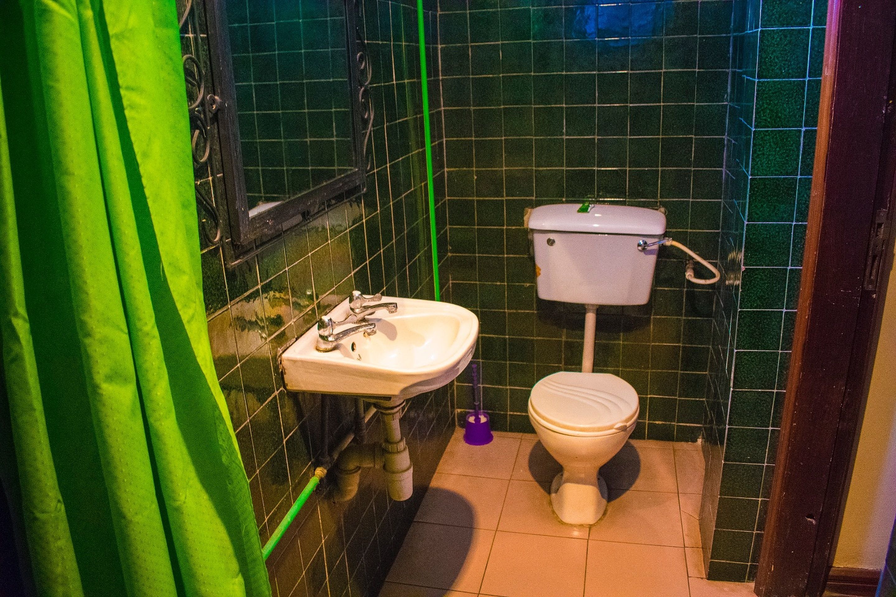 A small bathroom with a toilet and a sink, green tiles on the walls, and a green curtain.
