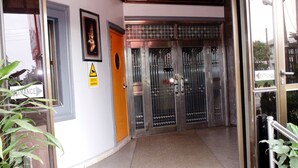 L’entrée d’un hôtel, avec un portail en métal, un panneau jaune indiquant un danger et un tableau encadré accroché au mur.