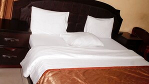 Un lit bien fait, avec du linge de lit blanc et un élément décoratif marron au pied du lit.