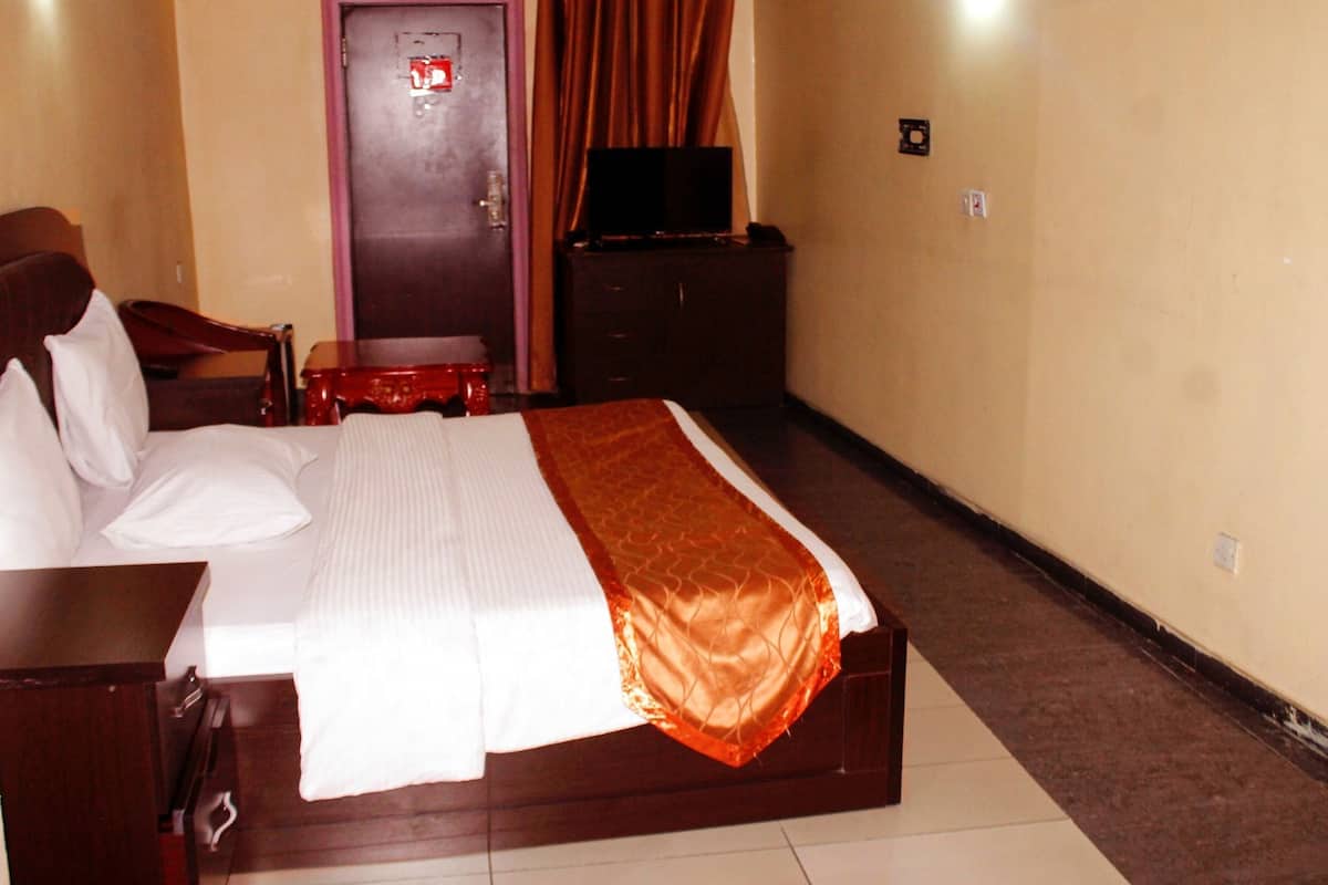 A hotel room with a bed, a desk, a chair, a television, and a wardrobe.