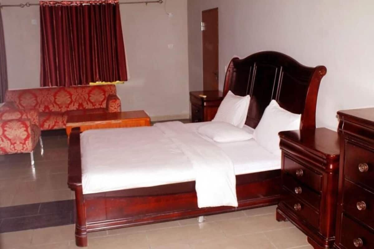 A bedroom with a wooden bed, a nightstand, a dresser, a red patterned sofa, and a curtain.