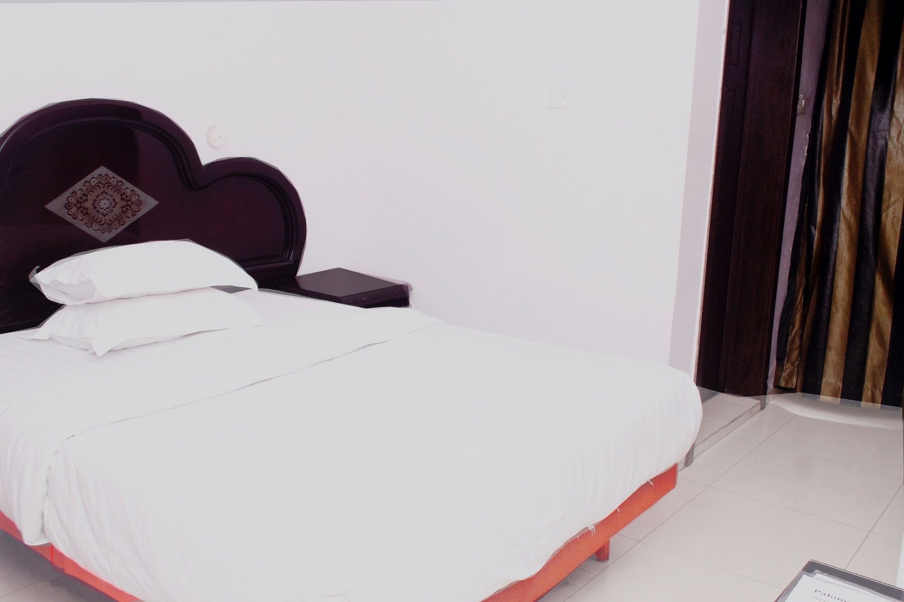 A neatly made bed with white bedding and a dark headboard with a decorative panel.