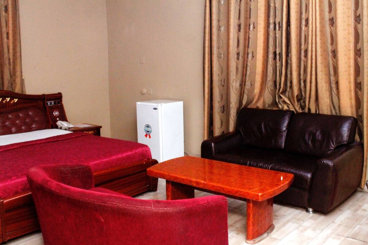 Una habitación de hotel con una cama, un refrigerador pequeño, un sofá de cuero y una mesa de centro de madera.