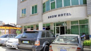 Um hotel com uma placa indicando "BNOW HOTEL" e vários carros estacionados na frente.