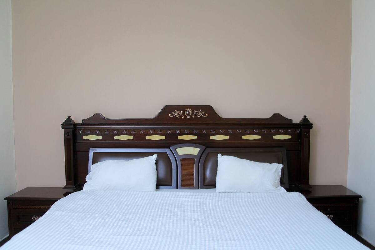 A neatly made bed with a wooden headboard, two bedside tables, and a plain wall.